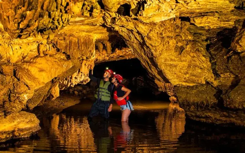 Visitantes con linterna caminando con el agua a los pies dentro de la Cueva del Indio