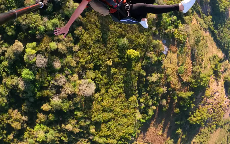 Pasajero y piloto en parapente sobre el bosque y los potreros del valle de Curití
