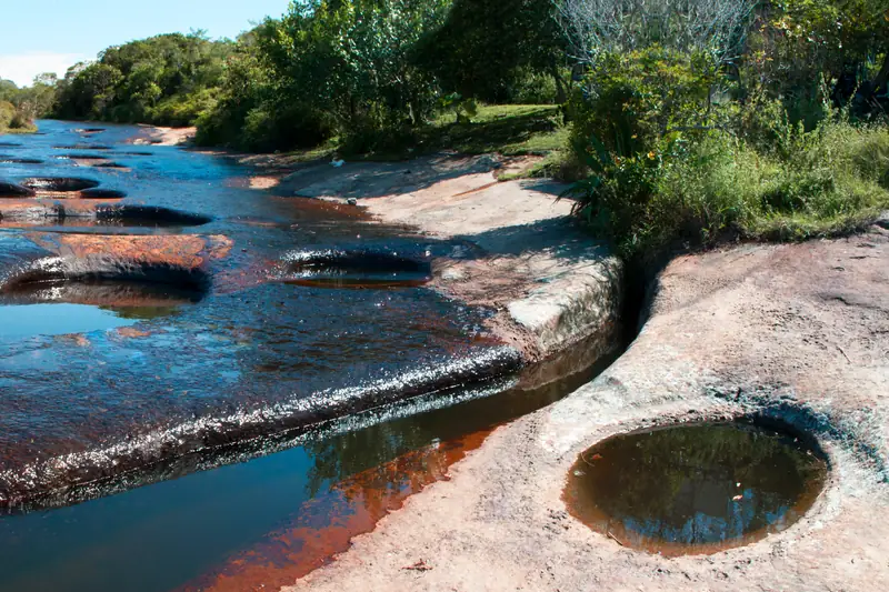 Agua de la quebrada Las Gachas sobre la laja rojiza, con pozos en la piedra y árboles en la orilla, en Guadalupe