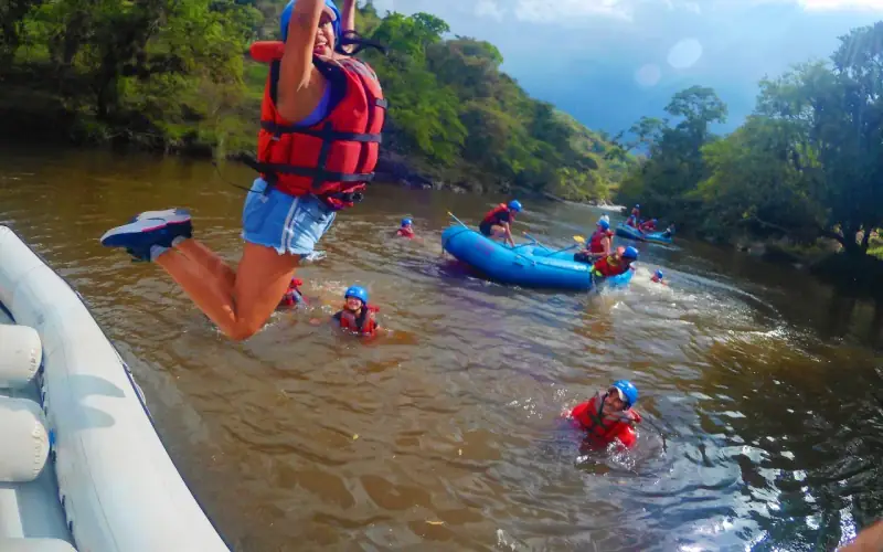 Remero con chaleco rojo saltando de la balsa al río Fonce, con más balsas atrás