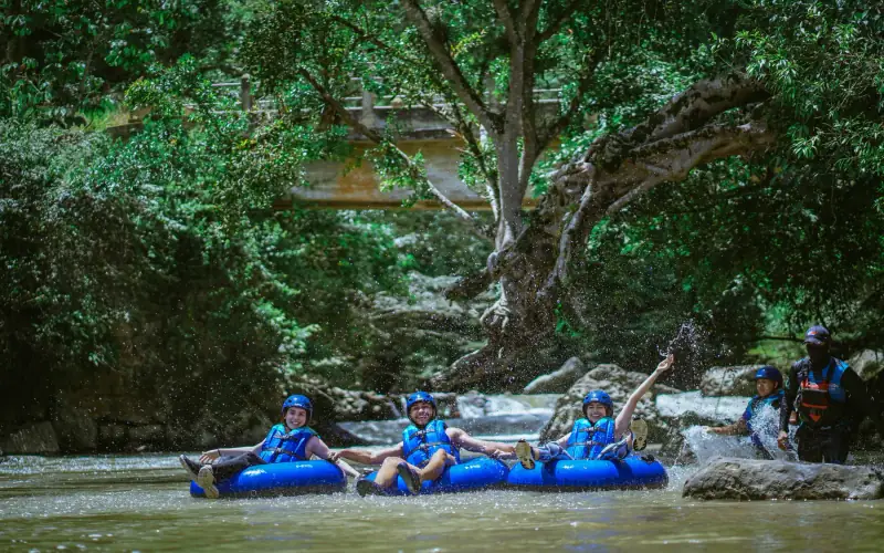 Tres personas con casco bajando el río en donas inflables bajo los árboles